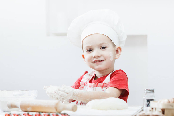 Flour is poured onto the table. Boy with chef hat preparing the pizza dough - kneading and stretching - Фото, изображение