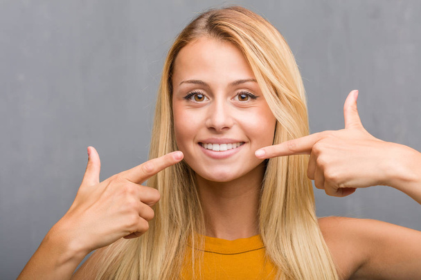 portrait of natural young blonde woman smiling and pointing at mouth - Foto, afbeelding