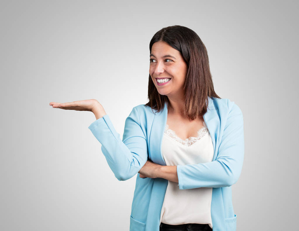 Женщина средних лет держит что-то руками, показывает продукт, улыбается и веселится, предлагая воображаемый объект
 - Фото, изображение