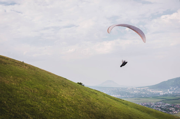 A white-orange paraglider flies over the mountainous terrain - Foto, immagini