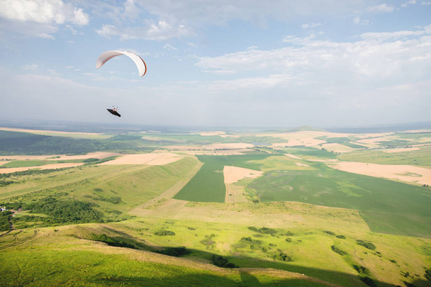 A white-orange paraglider flies over the mountainous terrain - Foto, imagen