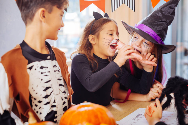 Two girls wearing Halloween costumes trying sweet hand Halloween cookie - Foto, Imagen