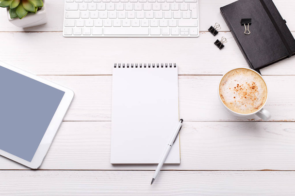 Werkruimte met toetsenbord dagboek pen paperclips en sappige koffie tablet op witte woden achtergrond plat leggen - Foto, afbeelding