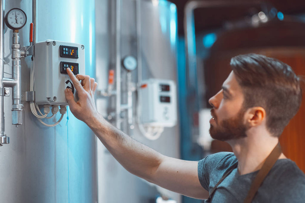 Young Brewer adjusts temperature sensors on beer tanks. - Fotó, kép