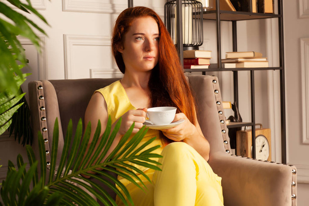Beautiful woman in a yellow suit with a cup sitting in a chai - Foto, Imagen