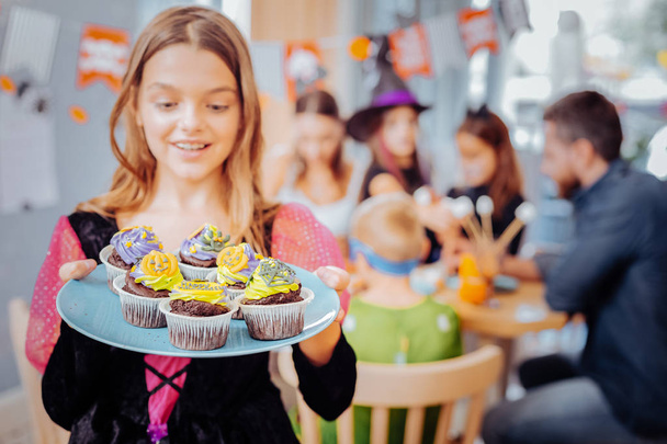 Funny happy girl feeling excited looking at plate with nice bright cupcakes - Zdjęcie, obraz
