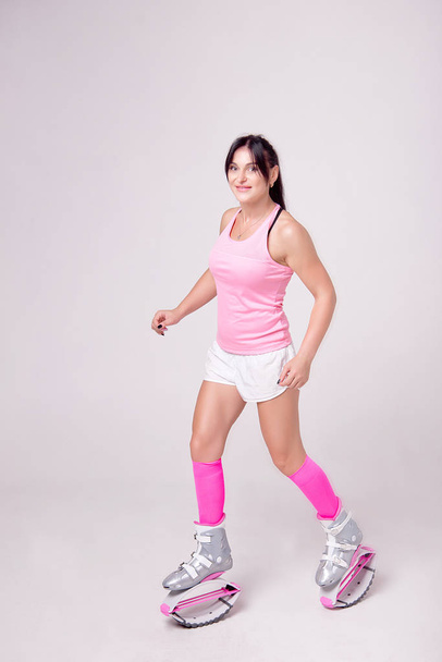 Beautiful athletic woman wearing in sports style clothing with kangoo jumps boots on her legs makes sports exercise in the gym. - Φωτογραφία, εικόνα