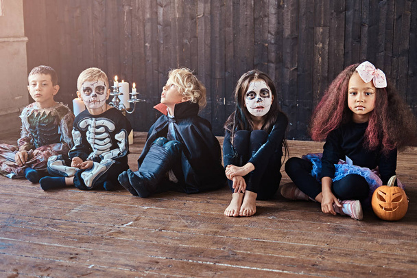 Хеллоуїн вечірка з груповими дітьми, які сидять разом на дерев'яній підлозі в старому будинку. концепція Хеллоуїна
. - Фото, зображення