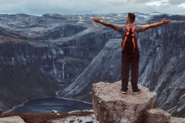 Tourist stands on the peak of the mountain with an amazing view of the Norwegian fjord. - Photo, Image