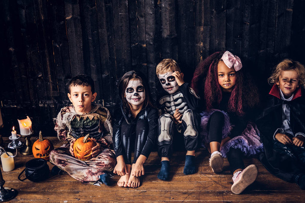 Halloween party z grupa dzieci którzy siedzieli na drewniane podłogi w starym domu. Koncepcja Halloween. - Zdjęcie, obraz