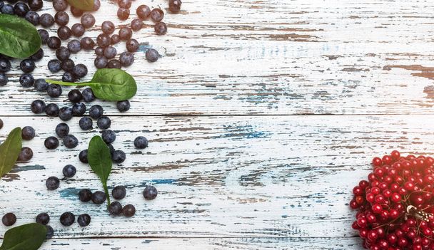 Blueberries and a bunch of red currants on vintage wooden white background. Light effects from the top view, copy space - Photo, image
