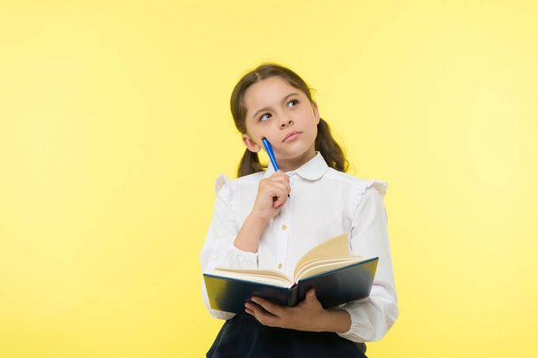 Girl cute schoolgirl in uniform hold book or textbook yellow background. Diligent pupil get knowledge from book. Child wear school uniform prepare for lesson her knowledge. Complex knowledge - Photo, image