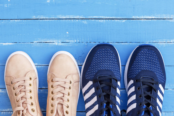 δύο ζεύγη των αρσενικών και θηλυκών αθλητικά παπούτσια σε μπλε φόντο ξύλινων σανίδων, κάτοψη - Φωτογραφία, εικόνα