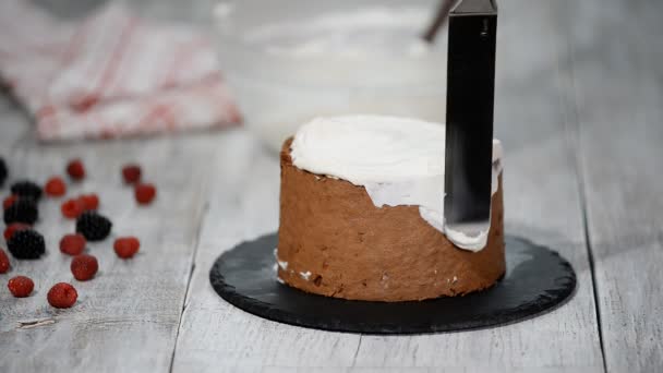 Close up of hands smearing butter cream on chocolate cake by white spatula. - Imágenes, Vídeo