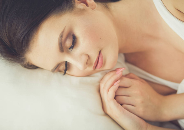 Beautiful young woman lying on white bed - 写真・画像