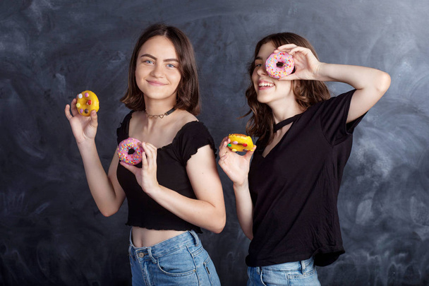 Happy pretty teenage girls with donuts having fun. Portrait of joyful girls with donuts on black background. Good mood, diet concept. - Foto, Imagen