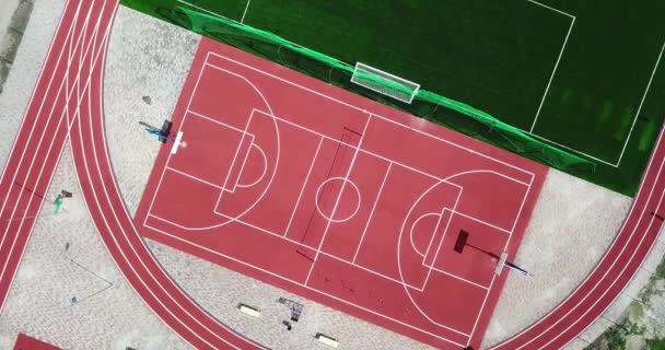 Üres játszótér sportstadion madártávlatból a része. Piros sport földön nagy tenisz és kosárlabda és labdarúgó zöld futballpálya, és fut az utakon. - Felvétel, videó