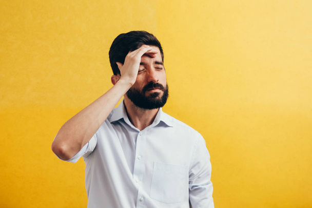 Portrait of an annoyed middle aged man suffering from a headache isolated over yellow background - Fotoğraf, Görsel