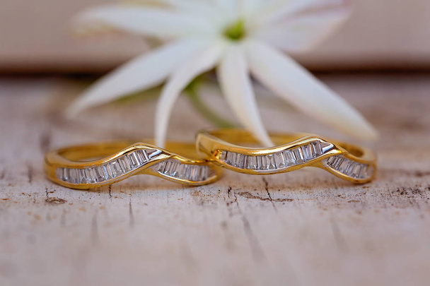 Diamond emerald cut wedding and eternity rings placed side by side on timber with a white flower in the background - Photo, Image