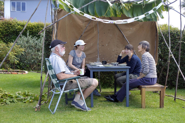 Еврейская семья, родители и дочери, сидя в Сукке в Суккот праздник кущей еврейский праздник в домашнем саду
. - Фото, изображение