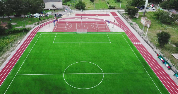 Lege speelplaats stadion met rode sport grond voor spelen grote tennis, basketbal en voetbal groen voetbalveld en uitvoeren van wegen. - Video