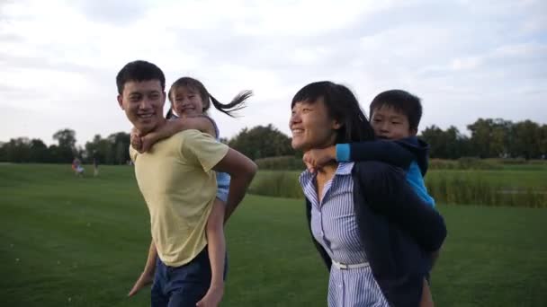Aasian vanhemmat antavat lapsille reppuselässä ratsastaa puistossa
 - Materiaali, video