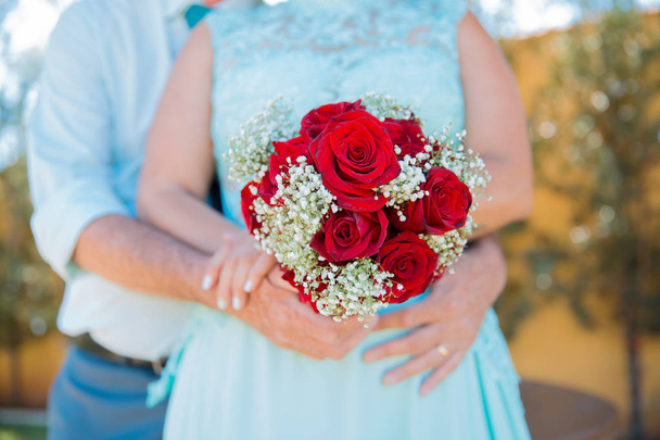 Bruid, houden een bruiloft boeket van bloemen (rode rozen). Gouden trouwringen. Bruids trouwjurk. Hand van een meisje met een boeket bloemen. bloemen op de huwelijksdag - Foto, afbeelding