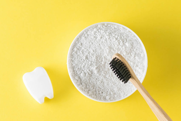 A jar of tooth cleaning powder, a wooden toothbrush and a tooth figurine on a yellow table. Oral care products. The view from the top. Flat lay. - Photo, Image
