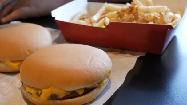 Teenager is eating fried french fries with onions and cheese. Hand punctures a plastic fork with unhealthy food or fast food next to large cheeseburgers - Footage, Video