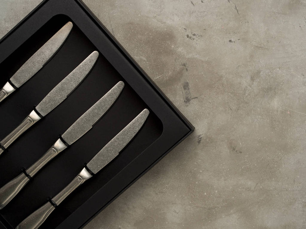 Top view of silver collection of knives in black box on grey concrete background - Foto, imagen