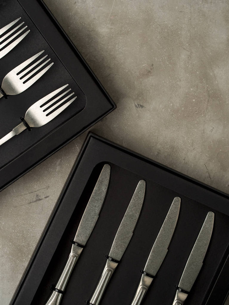 Top view of silver collection of forks and knives in black boxes on grey concrete background - Foto, immagini