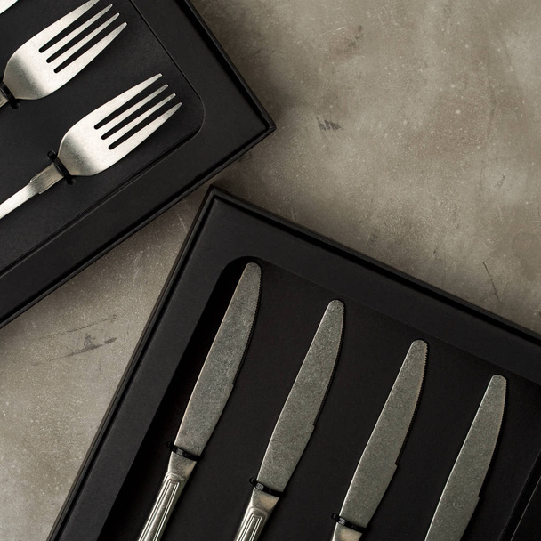 Top view of silver collection of forks and knives in black boxes on grey concrete background - Фото, изображение