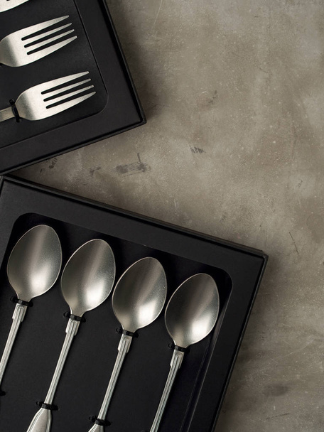 Top view of silver collection of forks and spoons in black boxes on grey concrete background - Фото, изображение