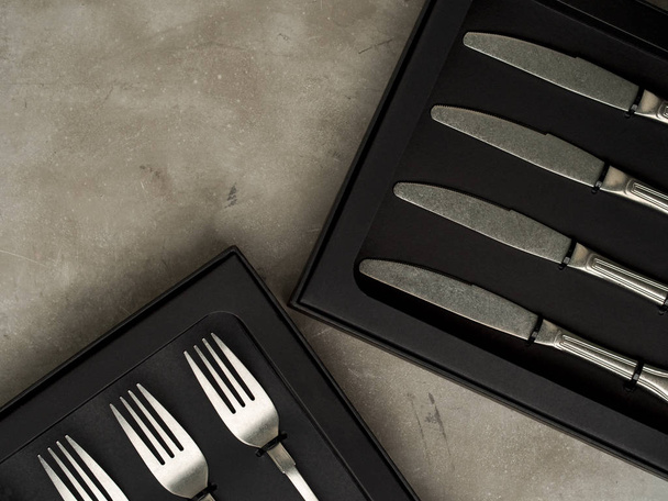 Top view of silver collection of forks and knives in black boxes on grey concrete background - Photo, Image