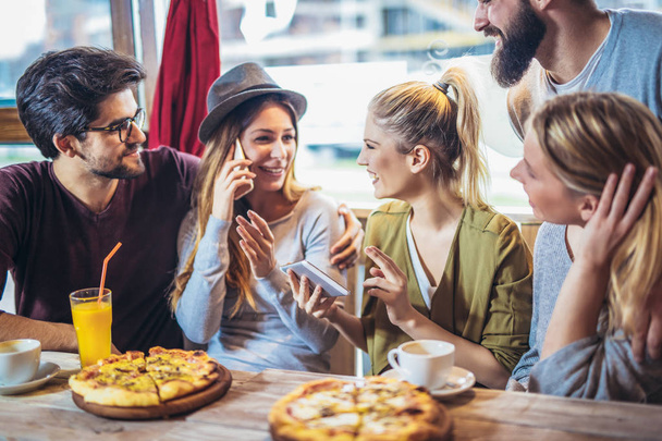 Young friends sharing pizza in a indoor cafe - Foto, afbeelding