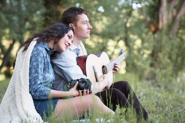 Genç çift ormanda oturan ve iskambil gitar, yaz doğa, parlak güneş ışığı, gölgeler ve yeşil yaprakları, romantik duygular - Fotoğraf, Görsel