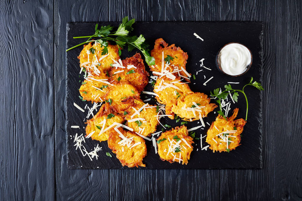 parmesan pumpkin fritters with sour cream, seasoned with fresh parsley leaves on the stone board on the black wooden table , top view - Photo, Image