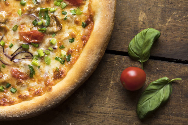 A pizza with spring onions, cheese, dried tomatoes on a vintage wood surface - Photo, Image