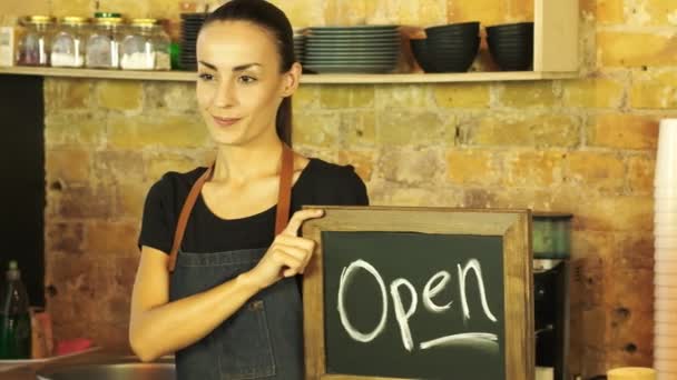 A coffee shop worker holds a Open sign and looks at the customer. - Filmati, video