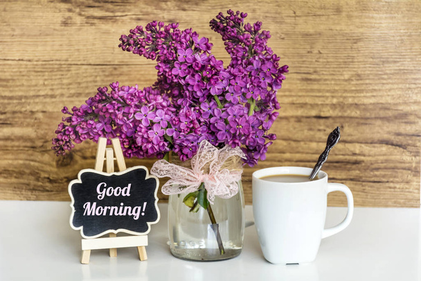 Bouquet of Lilac with Alarm Clock,Cup of Coffee and Good Morning Text on  Wooden Background .Spring Morning Concept - Foto, afbeelding