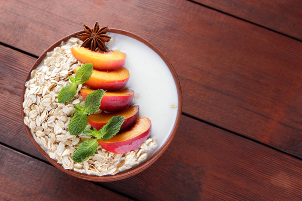 Oatmeal with fruits and green mint. Oat flakes with milk on wooden background. Healthy food. Breakfast for vegan. Dry oats with peaches, anise and milk. Copy space - Photo, Image