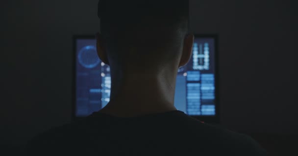 Male hacker works on a computer with maps and data on display screen in dark office room. - Felvétel, videó