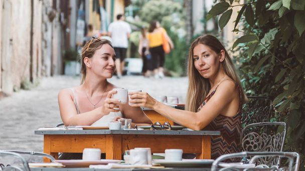 Two happy smiling women drinking something in Italian restaurant or cafe - female friendship and vacation in Italy concept - Фото, изображение