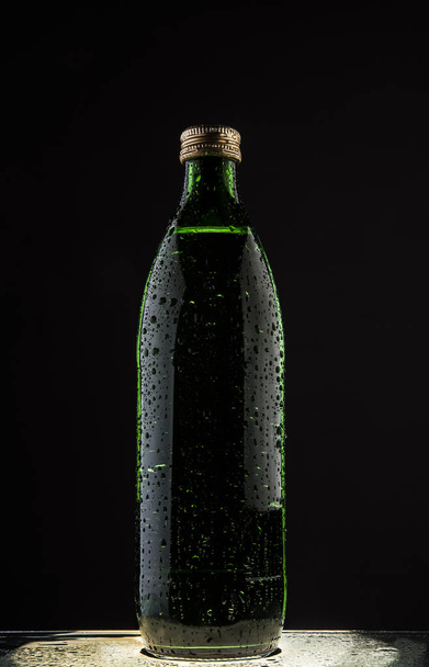 one wet green bottle with mineral pure water isolated on black background. drops on surface.  - Foto, Imagen
