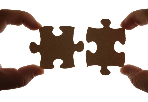 Fingers holding two pieces of brown wooden puzzle. Isolated on white background.  - Photo, Image
