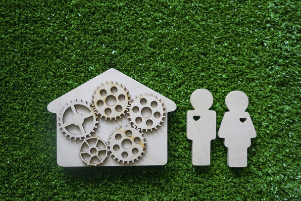 top view of wooden eco house with gears and couple figures on green grass background.   happy family concept with copy space - Foto, imagen