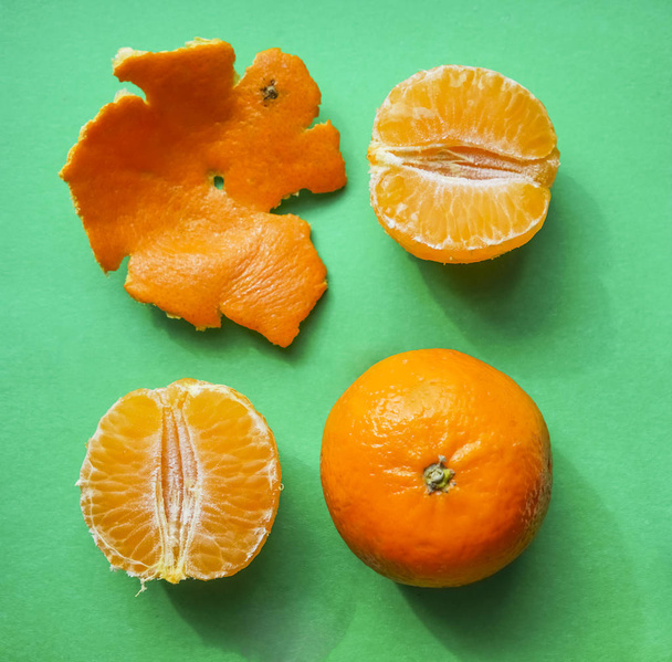 Fresh mandarins on green paper background, crust and tasty sweet slices - Photo, image