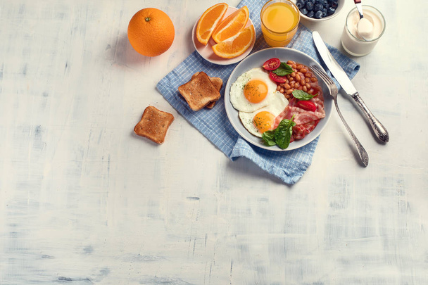 Plate of breakfast with fried eggs, bacon, beans, orange juice and toasts. Top view with copy space - Foto, imagen