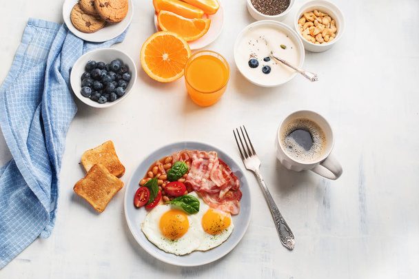 Breakfast with fried eggs, bacon, orange juice, yogurt and toasts. - Foto, Bild