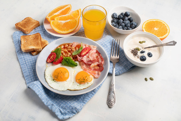 Plate of breakfast with fried eggs, bacon, beans, orange juice and toasts.  - Foto, imagen